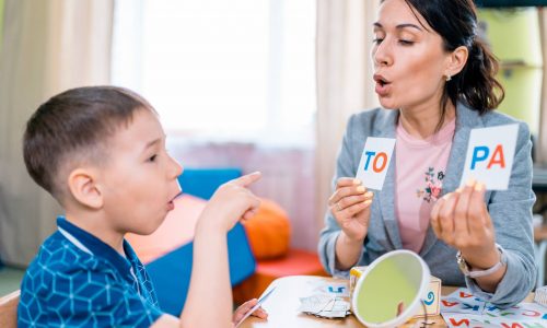 The attractive woman teacher teaches the preschool aged boy to read. The woman is holding the cards with the letters and the boy is trying to read them (The attractive woman teacher teaches the preschool aged boy to read. The woman is holding the card