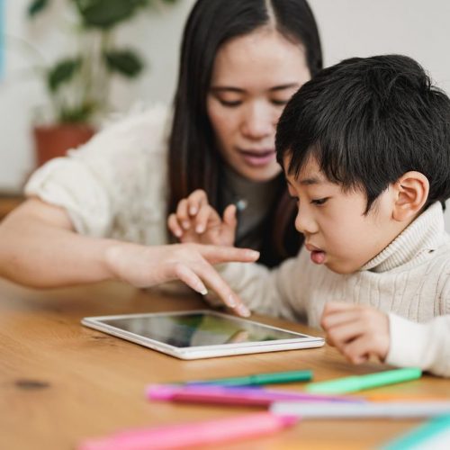 Asian nanny and preschool child learning with digital tablet indoor - Daycare and technology concept